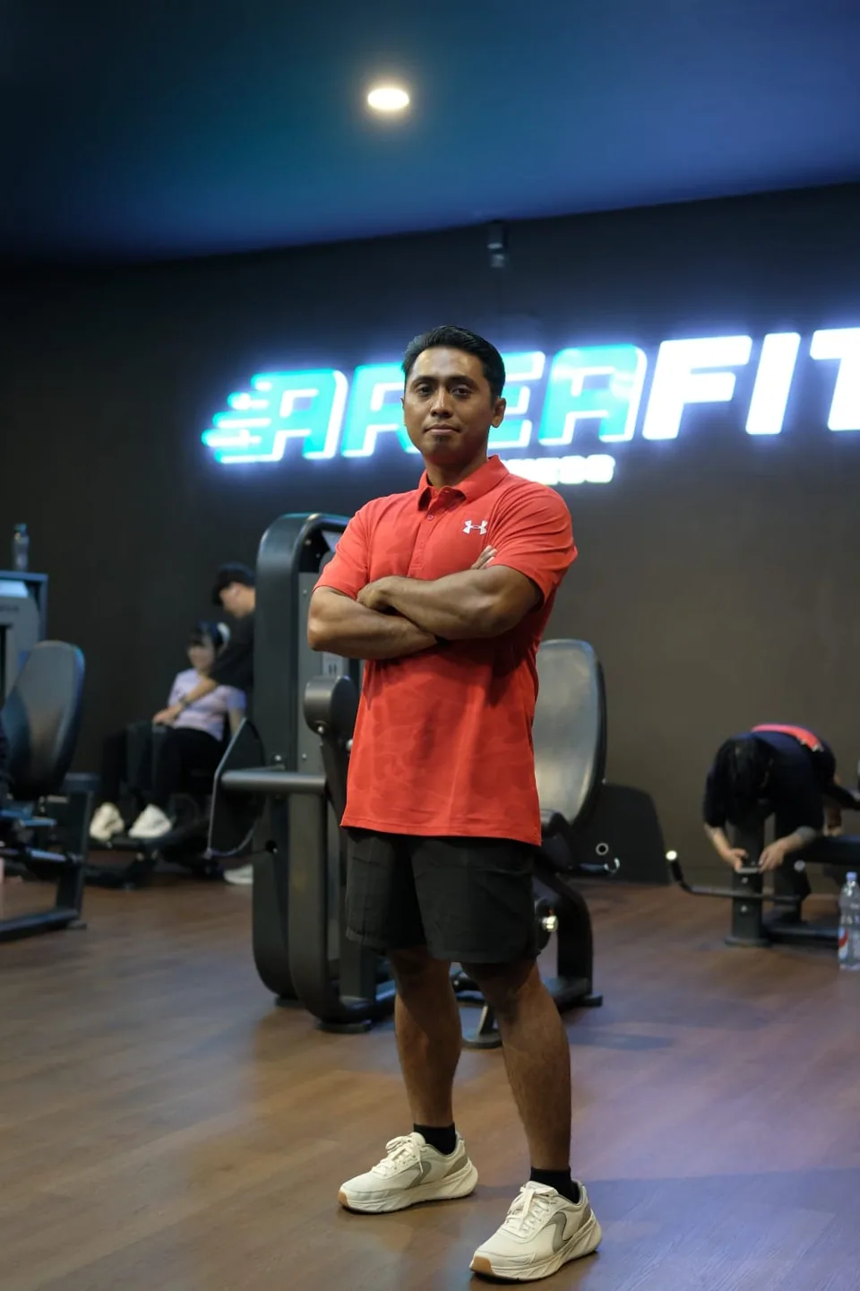 Coach Erik berdiri bersedekap dengan kaus merah di AreaFit.